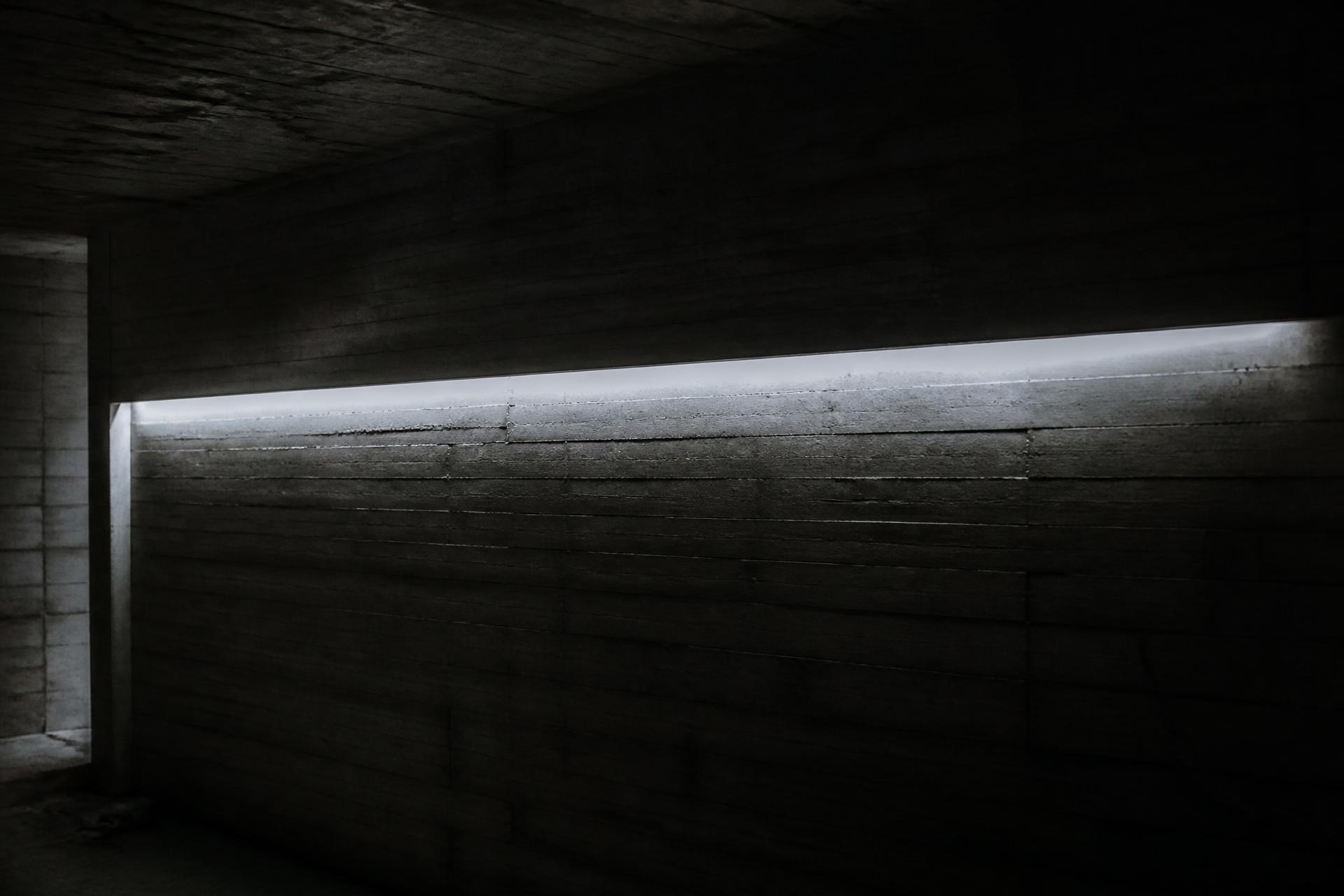 A single line of daylight cutting across a dark board-formed concrete interior